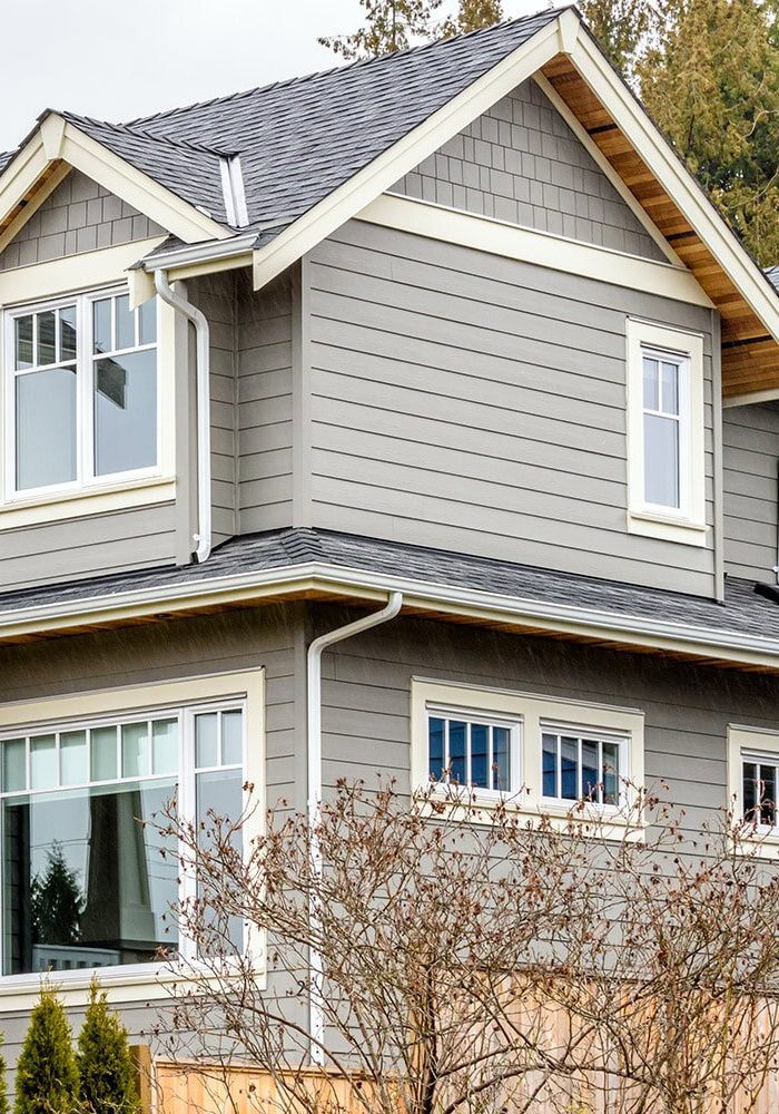 Gutter installation on a contemporary gray house with multiple windows and a sloped roof.